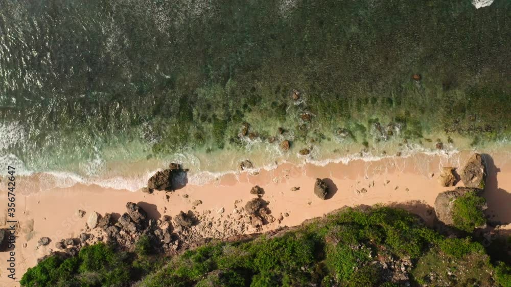 Top down aerial view from above of giant ocean waves crashing and foaming on empty sand tropical beach with big rock stones. Bird's eye aerial shot of golden beach meeting deep blue ocean water. Top down aerial view from above of giant ocean waves crashing and foaming on empty sand tropical beach with big rock stones. Bird's eye aerial shot of golden beach meeting deep blue ocean water.
