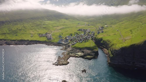 4k drone flight moving forvard and down footage (Ultra High Definition) of Gjogv village. Foggy summer scene of Eysturoy island. Bright panoramic seascape of Atlantic ocean, Faroe Islands, Denmark. photo