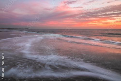Waves retreating back into the sea under a soft vibrant pink and orange sky. 