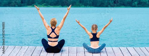 Foto Mother and daughter doing yoga at the shore of the lake in summer