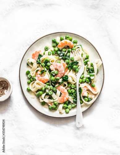 Delicious lunch - green peas, shrimps, spinach, cream sauce tagliatelle pasta on a light background, top view