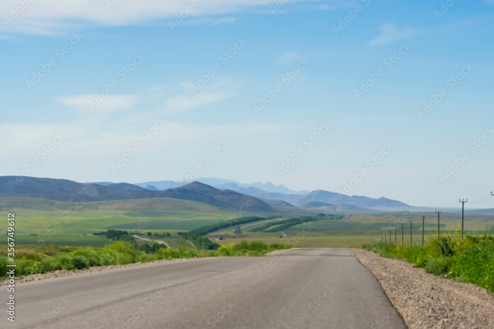 Highway and mountain landscape. Asphalt road, steppe and mountains in the distance. The road leading to the mountains. Green grass along the road. Summer piedmont landscape. Road perspective. Karatau 