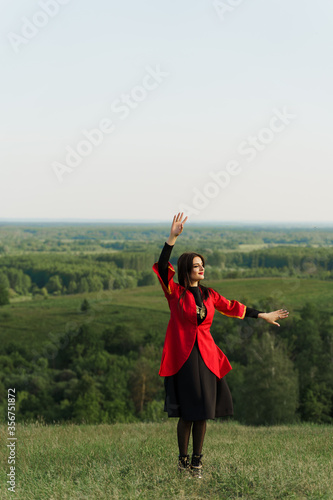 Georgian woman dances national dance in red national dress on the green hills of Georgia background. Georgian culture lifestyle.