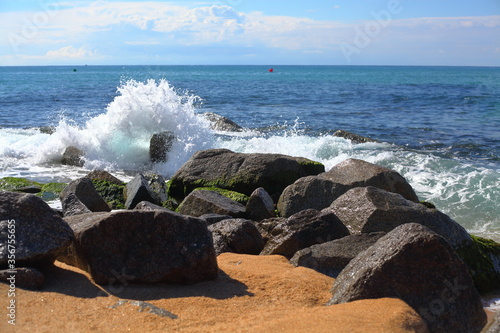 oleaje sobre rocas de escollera en playa arenosa photo