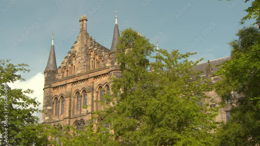Tilt up shot of people walking by trees near church in city against sky on sunny day - Glasgow, Scotland Tilt up shot of people walking by trees near church in city against sky on sunny day - Glasgow, Scotland