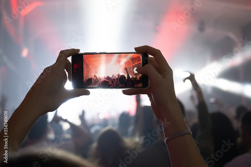 girl hands at a concert shoots videos and photos of the crowd and stage on a smartphone. music festival in the club. joyful moments