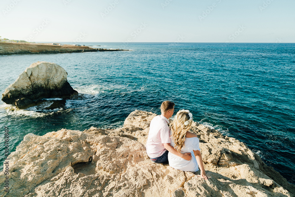 Back view just married couple standing on the rocks in front of the ocean. Just married view from behind. Honeymoon at the sea. High quality photo Back view just married couple standing on the rocks in front of the ocean. Just married view from behind. Honeymoon at the sea. High quality photo