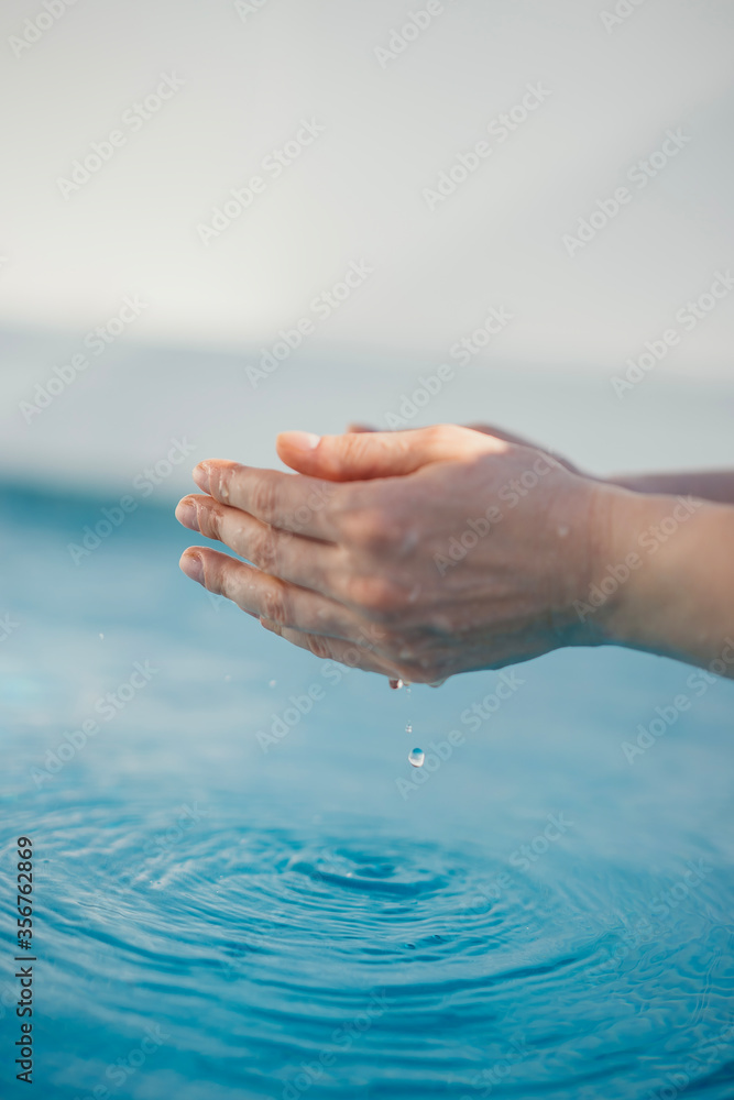 female hands with water over a blue pool
