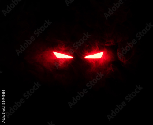 Ominous luminous eyes staring out of the darkness illuminate with rays of red light swirling white smoke
