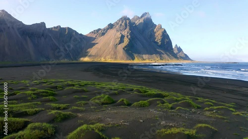 4k drone forward video (Ultra High Definition) of Stokksnes cape with Vestrahorn (Batman Mountain) on background. Panoramic Icelandic view of black sand dunes with fresh green grass. 