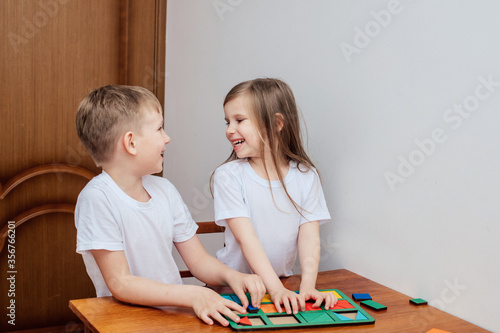 a boy and a girl of European appearance in light clothng sit and play a Board game photo