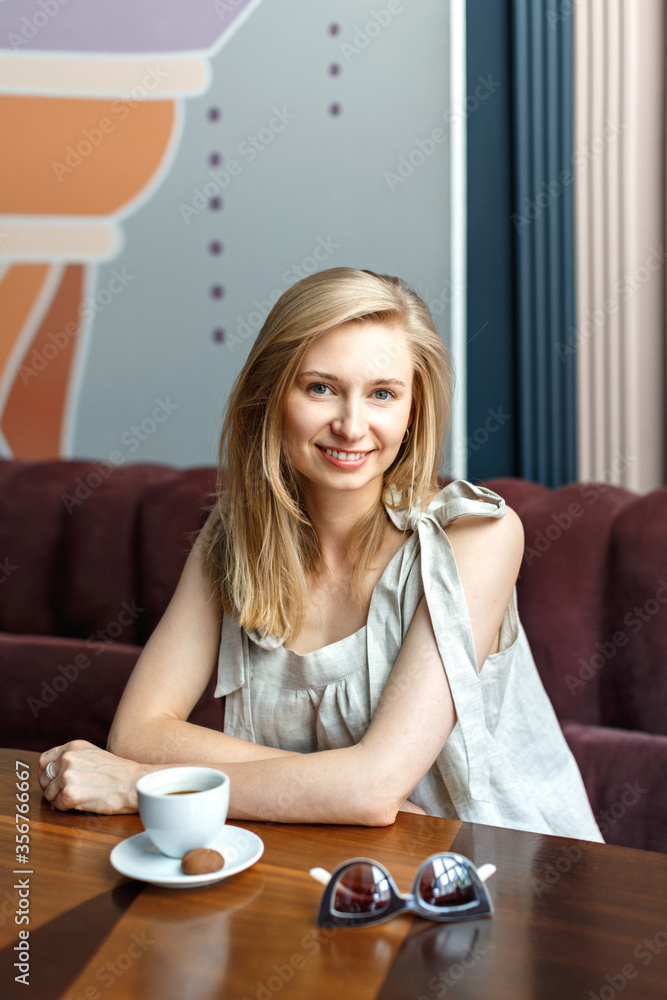 Happy young blond woman sitting in a cafe and drinking coffee during her lunch break. Female portrait Happy young blond woman sitting in a cafe and drinking coffee during her lunch break. Female portrait