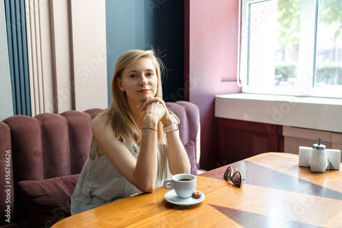 Happy young blond woman sitting in a cafe and drinking coffee during her lunch break. Female portrait