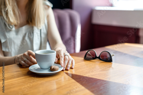 A young blond woman sits in a cafe and drinks coffee during her lunch break. Woman portrait without face