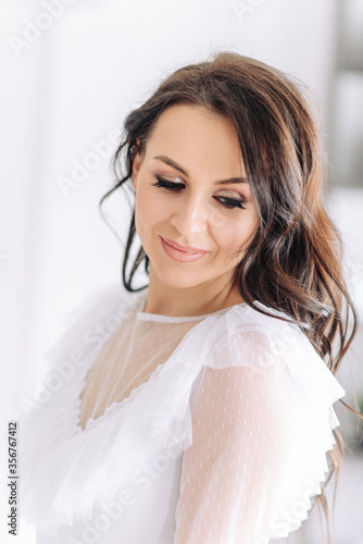 A beautiful and lovely brunette girl with perfect smooth skin and incredible brown eyes in a luxurious white dress smiles a bright and snowy smile. Light and airy vertical photo