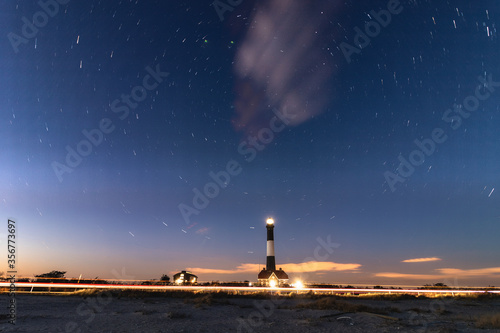 Circular star trails revolving around Polaris with a lighthouse beacon in the foreground. Fire Island lighthouse, New York. 