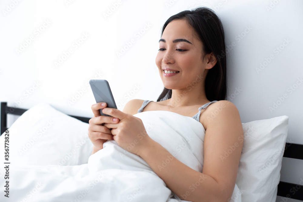 Smiling woman messaging on smartphone in bed Smiling woman messaging on smartphone in bed