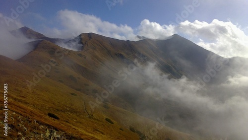 Mountain ridge with a mountain trail with white clouds on a sunny autumn day without people