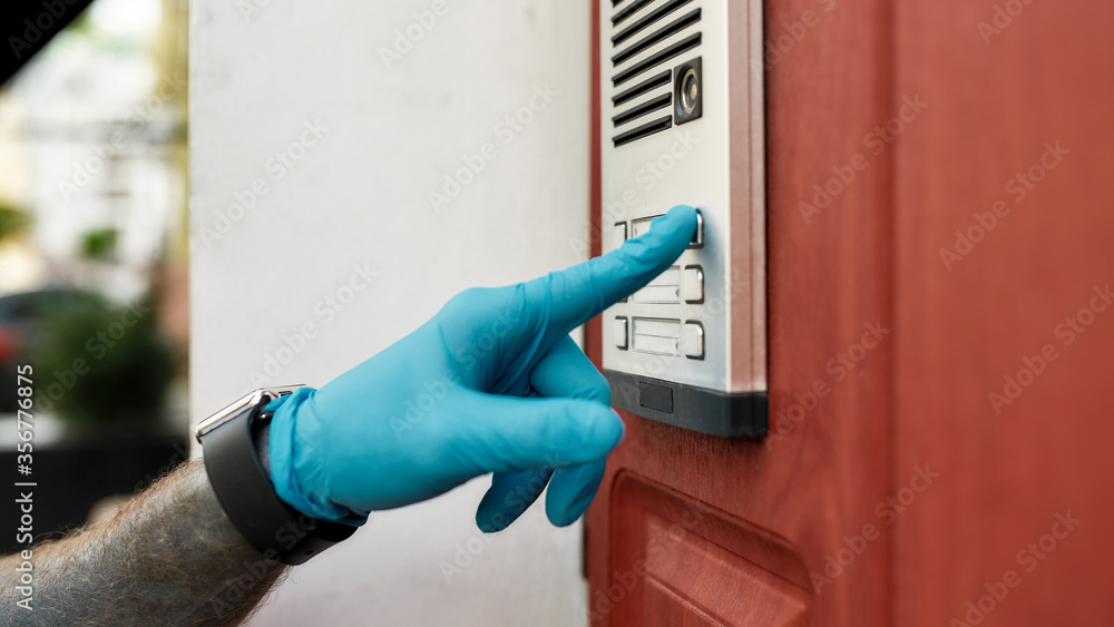 Close up of delivery man wearing gloves due to the emergence of the Covid19 virus, ringing a doorbell, while delivering food. Courier, delivery service, lockdown concept