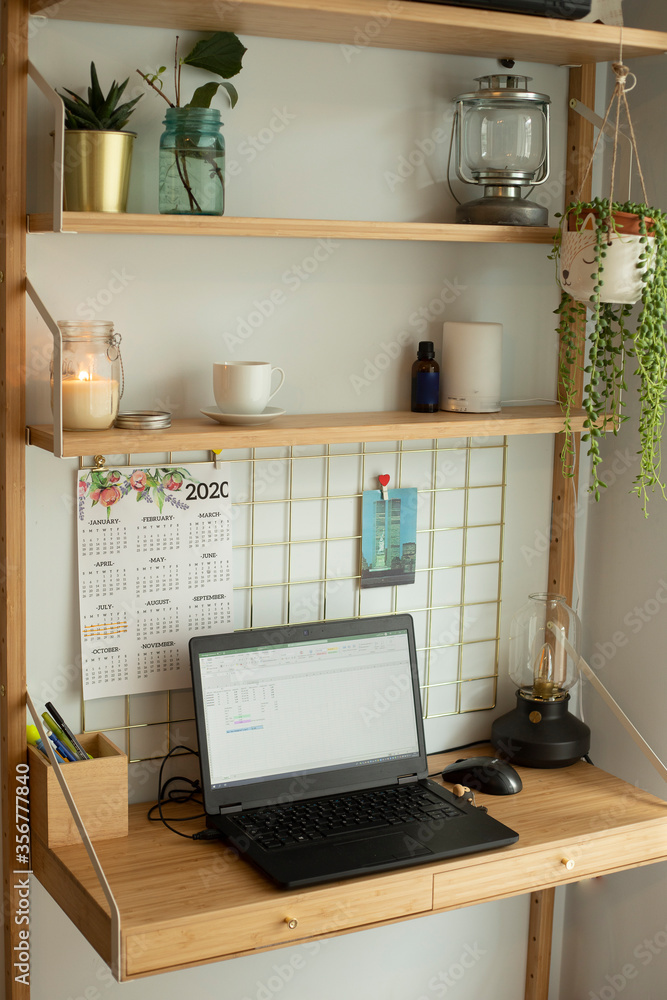 Small home office remote station, with laptop, houseplants, metallic board, candles and table lamp. Vertical shot. Small home office remote station, with laptop, houseplants, metallic board, candles and table lamp. Vertical shot.