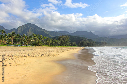 Hanalei Beach in Kauai, Hawaii. The view on the ocean waves. The empty sandy beach during covid 19 pandemic. The mountains with lush palm tree forest in the background.  photo