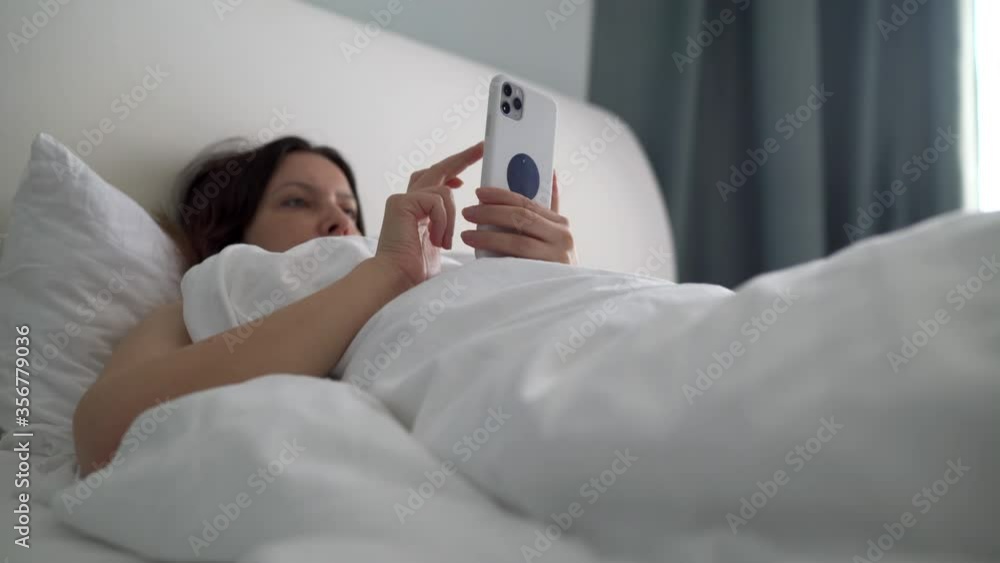 Woman holding mobile phone while lying in bed at home. Woman holding mobile phone while lying in bed at home.