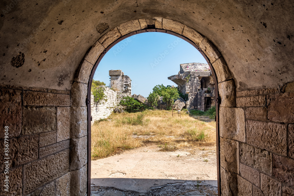 Ruins of Austro-Hungarian Fortification Fort Forno in Istra, Croatia. Looking out from arched stone passage hallway. Abandoned landmark dating back to 1904 covered with vegetation in bad shape