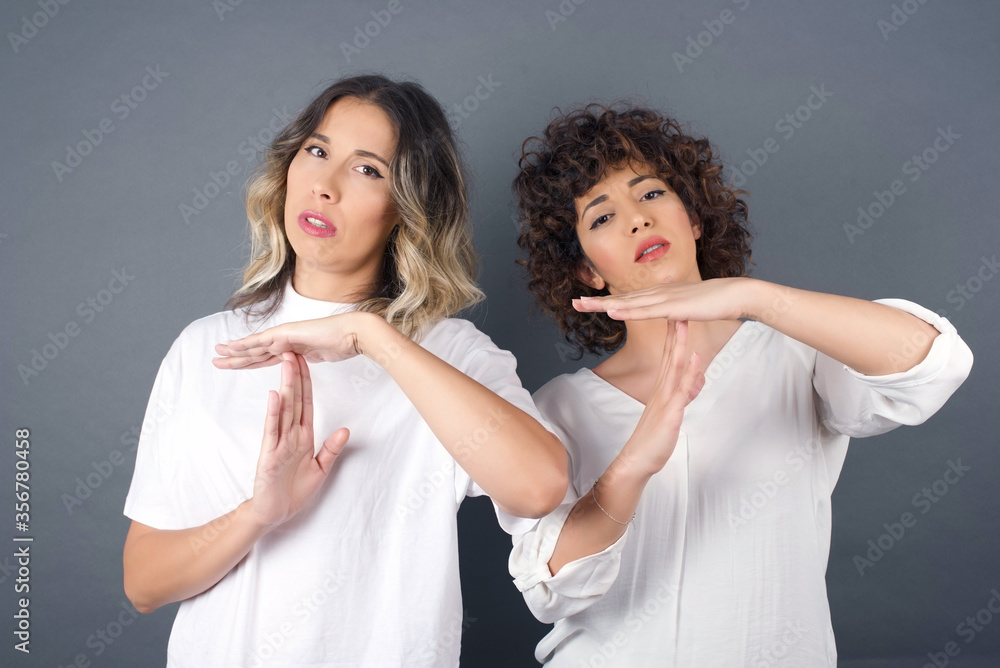 Young pretty girl friends tired and bored, making a timeout gesture, needs to stop because of work stress, time concept. Standing against gray wall. Young pretty girl friends tired and bored, making a timeout gesture, needs to stop because of work stress, time concept. Standing against gray wall.