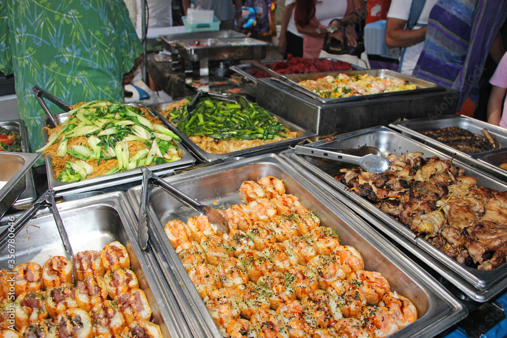 Hawaiian / Asian street food. Metal containers with sushi and barbecue meat with the side of noodles, veggies and salads.