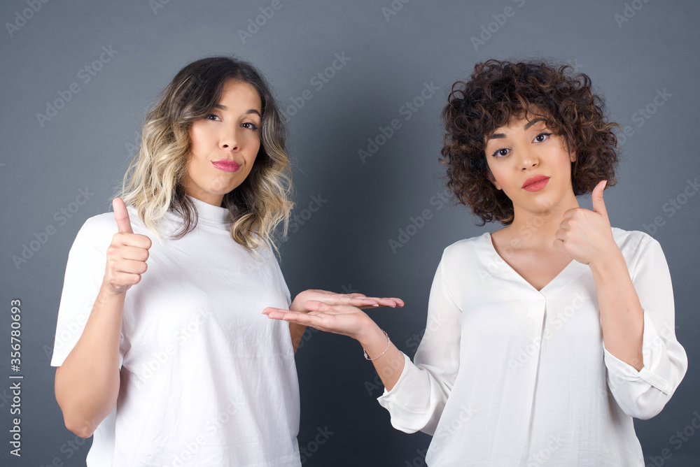 Young happy cheerful woman showing thumb up and pointing with the other hand while standing outdoors. Good Job. Wearing casual clothes. Young happy cheerful woman showing thumb up and pointing with the other hand while standing outdoors. Good Job. Wearing casual clothes.