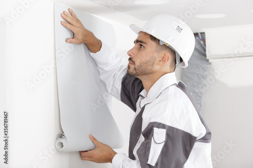 Slika na platnu young decorator holding roll of wallpaper against a wall