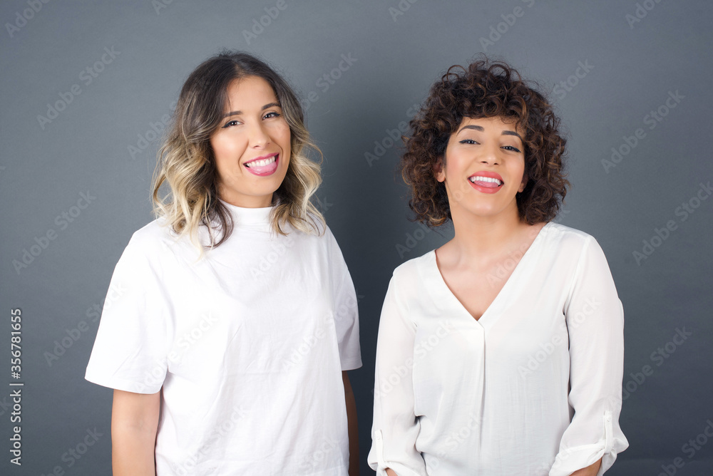 Beautiful Young caucasian woman with happy and funny face smiling and showing tongue. Wearing casual clothes and standing against gray studio background. Beautiful Young caucasian woman with happy and funny face smiling and showing tongue. Wearing casual clothes and standing against gray studio background.