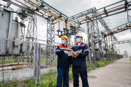 Engineers electrical substations conduct a survey of modern high-voltage equipment in the mask at the time of pandemia. Energy. Industry