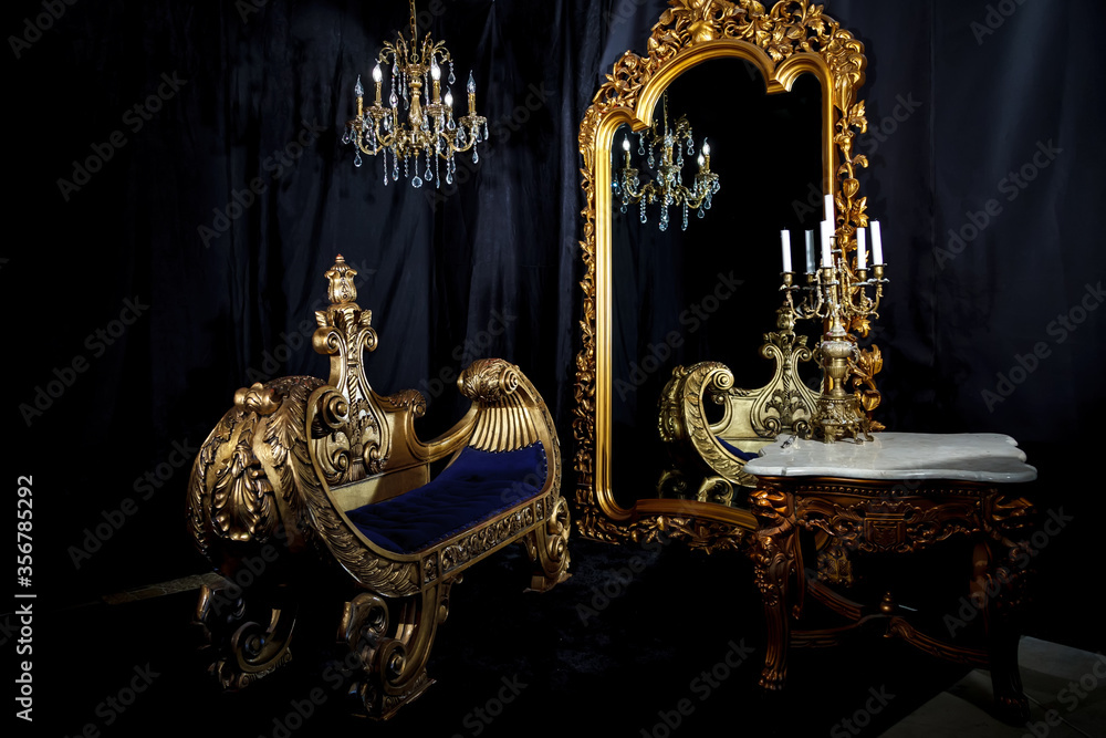 Vintage interior with antique furniture on black background. Old gondola sofa, chandelier and candelabra on table by huge mirror. Gold in black. Copyright space. Large space for inscription or logo