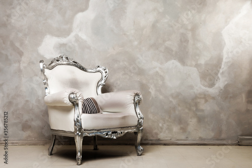 An antique white chair against wall. Antique leather chair. There is striped pillow on chair