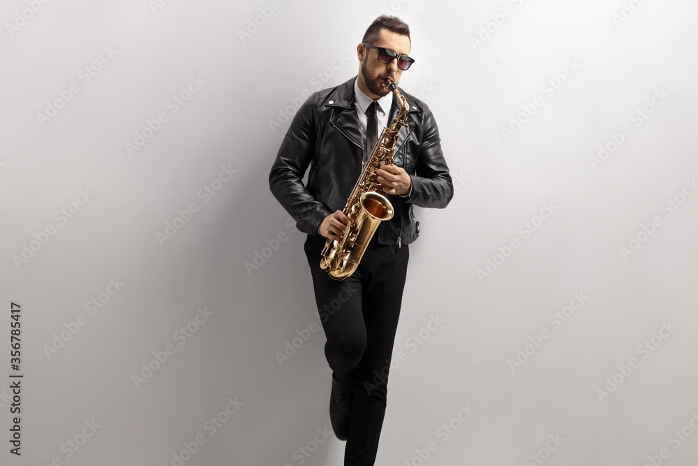Naklejka premium Man playing a saxophone and leaning on a gray wall