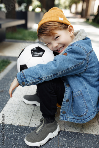 Photo of adorable little boy posing with soccer ball in street.