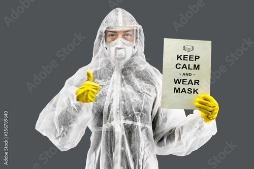 Doctors, infectionist, research and covid19 concept. Young european female doctor showing 'Keep Calm and Wear Mask' poster, wear face mask, gloves and protective clothes. photo