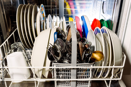 Clean dishes and cutlery inside a dishwasher at home.