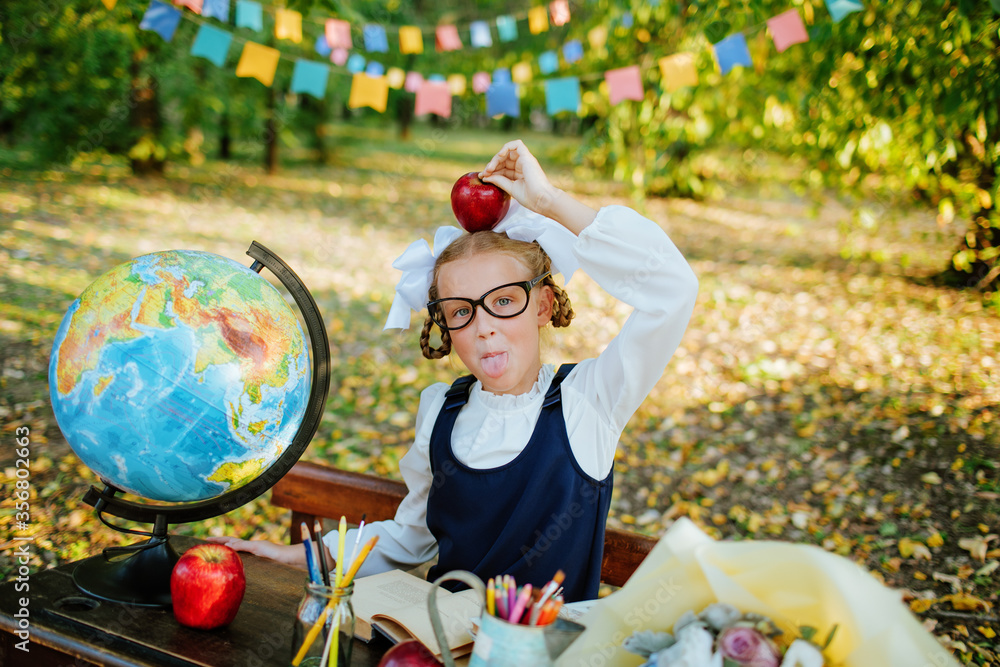 Fototapeta premium schoolgirl at a school desk holds on her head a newton's apple