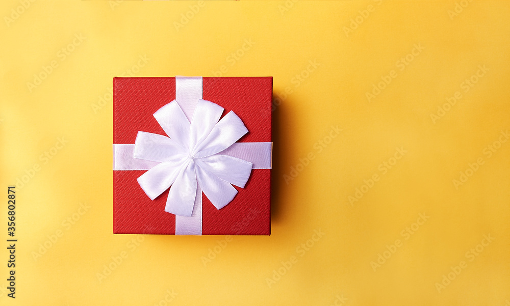 Decorative red gift box with white ribbon on yellow background. Top view. Space for text Decorative red gift box with white ribbon on yellow background. Top view. Space for text