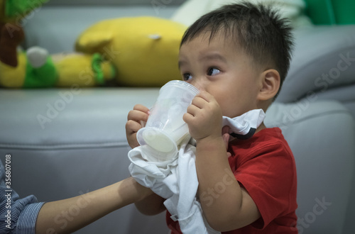 portrait of baby boy holding plastic cup drinking milk 