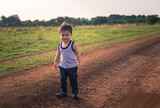 portrait of little asian boy standing on dirt road in the field during evening sunset in summer season 