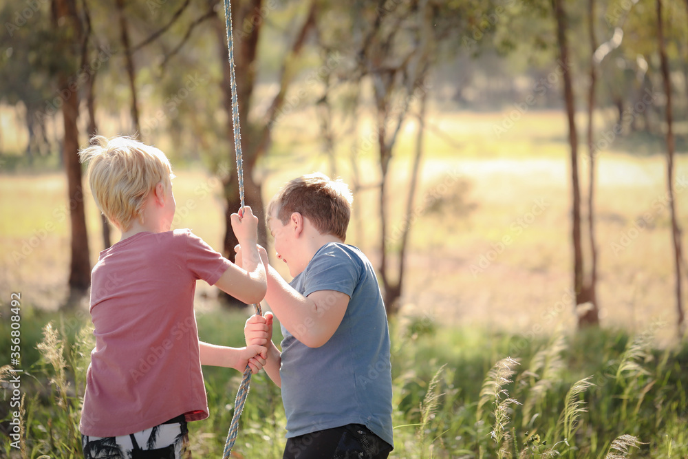 Fototapeta premium Two brothers playing on rope swing in beautiful bush location. Outdoor play during times of self isolation using imagination.