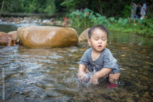 Cute little kid sitting and playing water in small water pond in natural parkland during family vacation in summer season