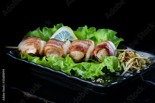 meat on wooden skewers, pork, chicken, fish, scallop, beef, shrimp in a black plate on a black background.