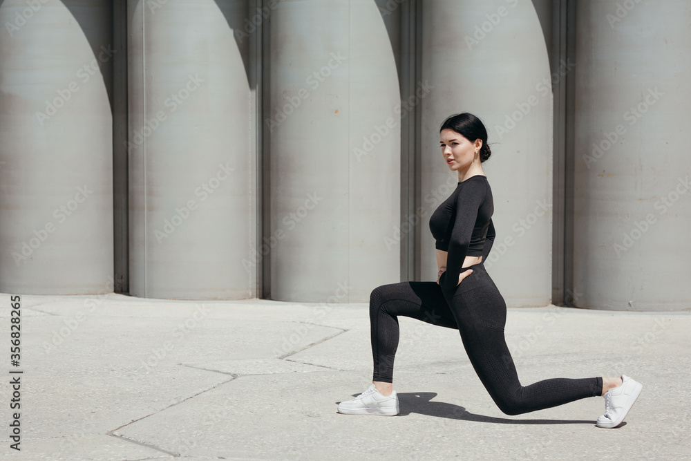The girl in a sports uniform sat down on her knee and doing stretching of her thigh muscles on the street in the park. The girl in a sports uniform sat down on her knee and doing stretching of her thigh muscles on the street in the park.