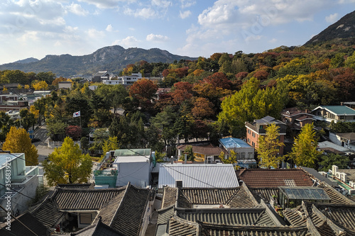 Rooftops of a traditional hanok village. Forest and hills at the background. Autumn leaves red and green. Bukchon hanok village. Seoul, South Korea, Asia