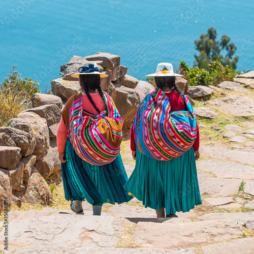 Indigenous Peruvian Quechua women in traditional clothing walking down steps on Taquile Island, Titicaca Lake, Peru. photo