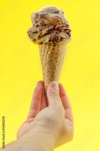 mão segurando casquinha de sorvete de caramelo sobre fundo amarelo